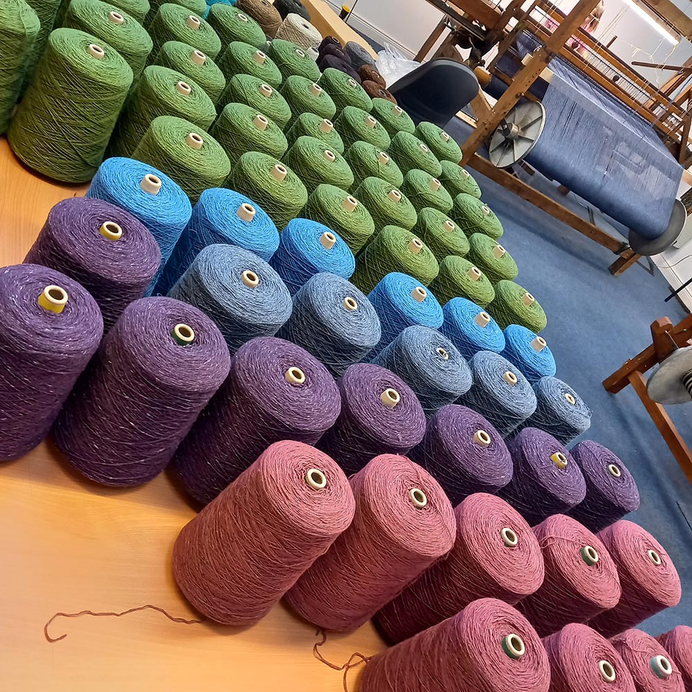 A colourful selection of woolen spools on the floor beside a loom.